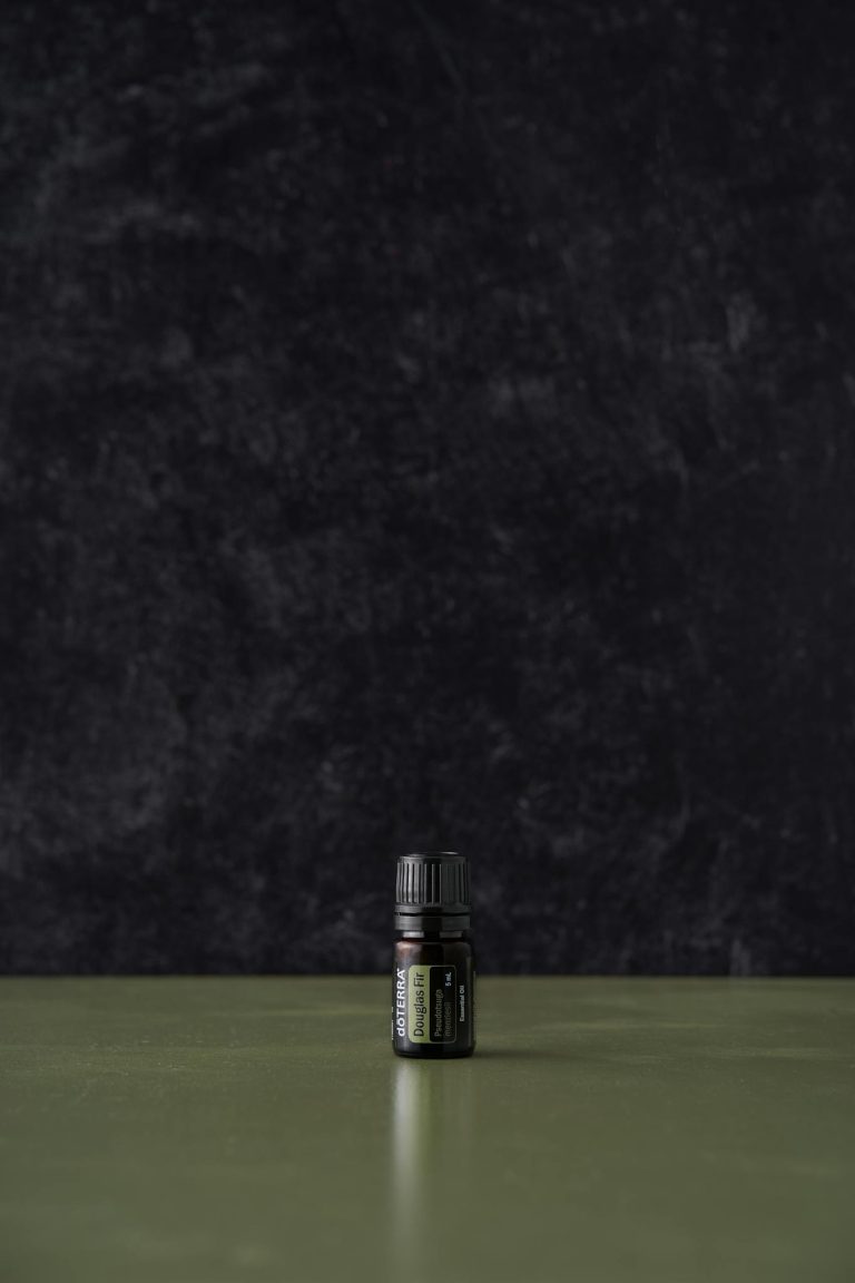 A minimalist image of a black essential oil bottle centered on a dark textured background.
