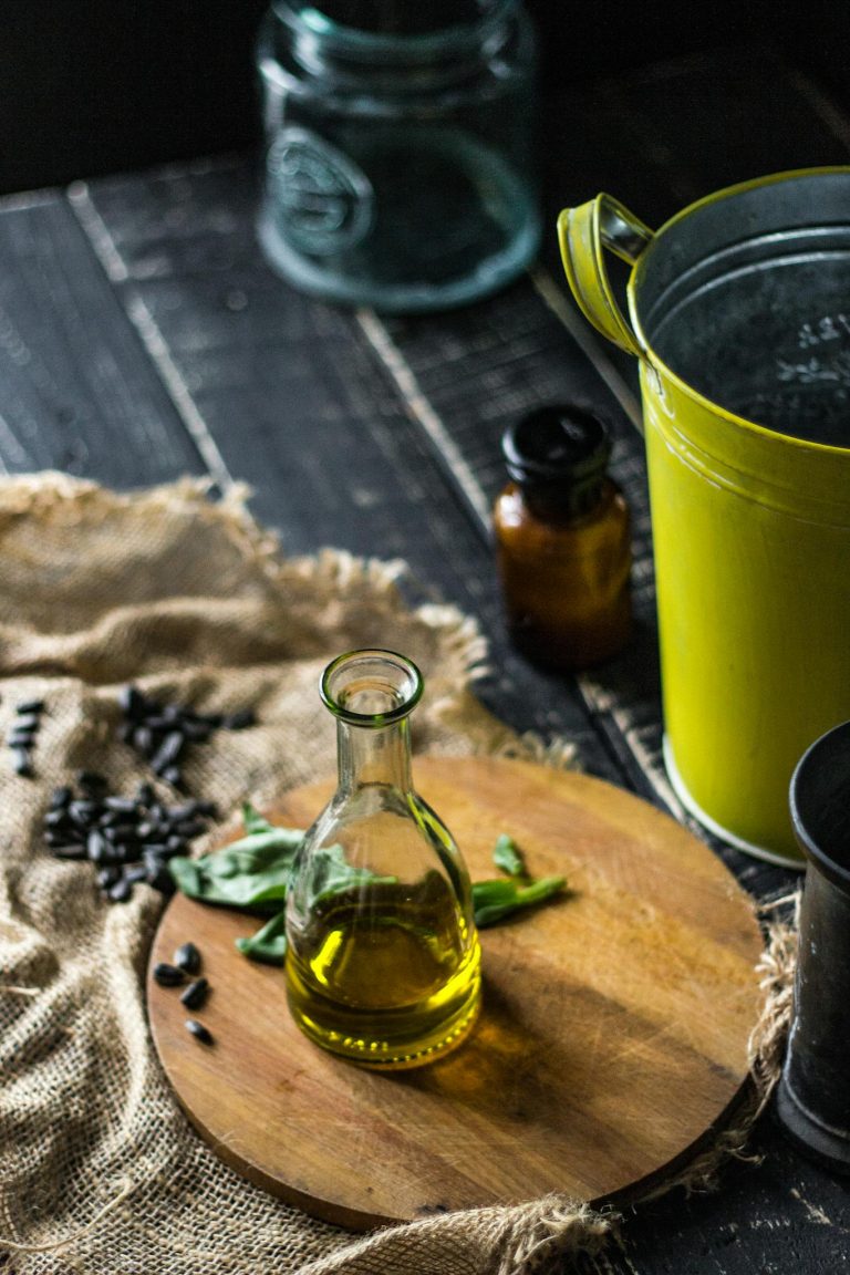 A rustic setup featuring an olive oil bottle on a wooden board with herbs and black seeds.