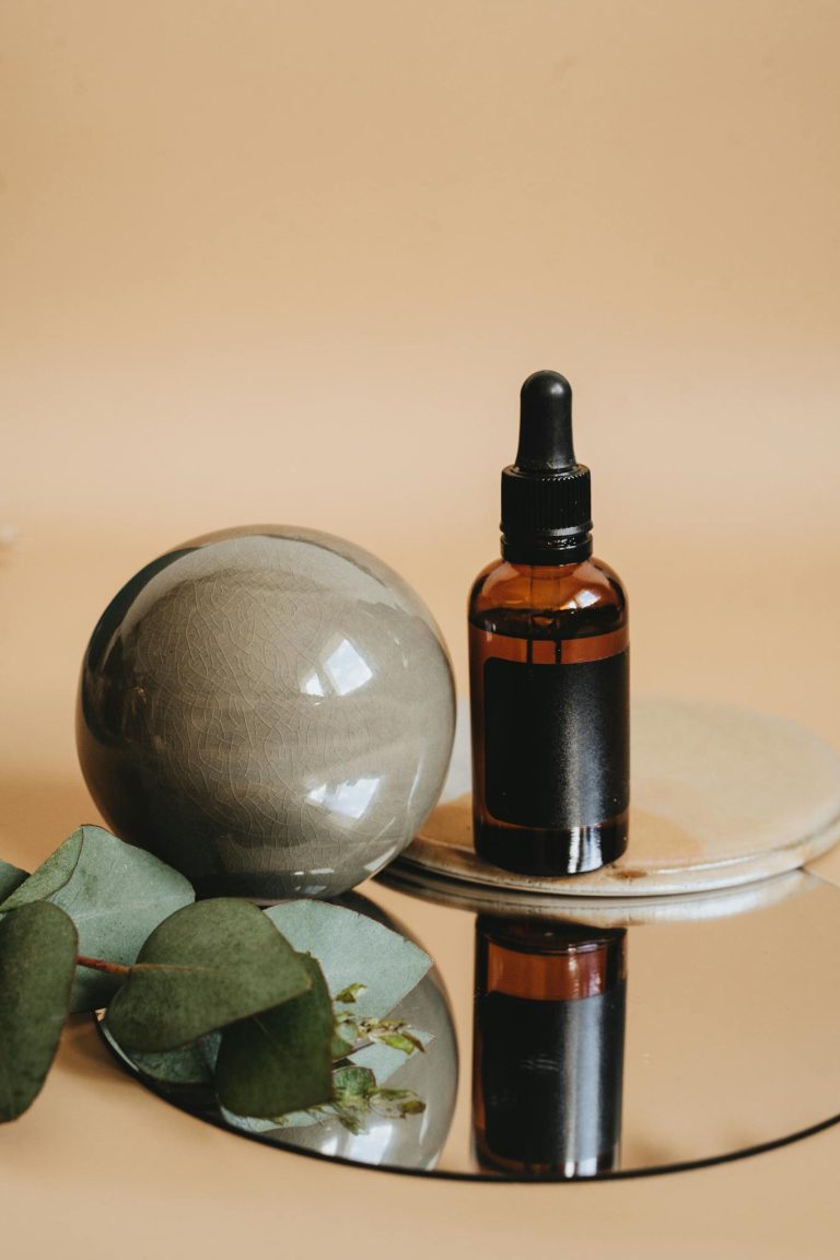 Aromatherapy oil bottle with eucalyptus leaves on a reflective surface.
