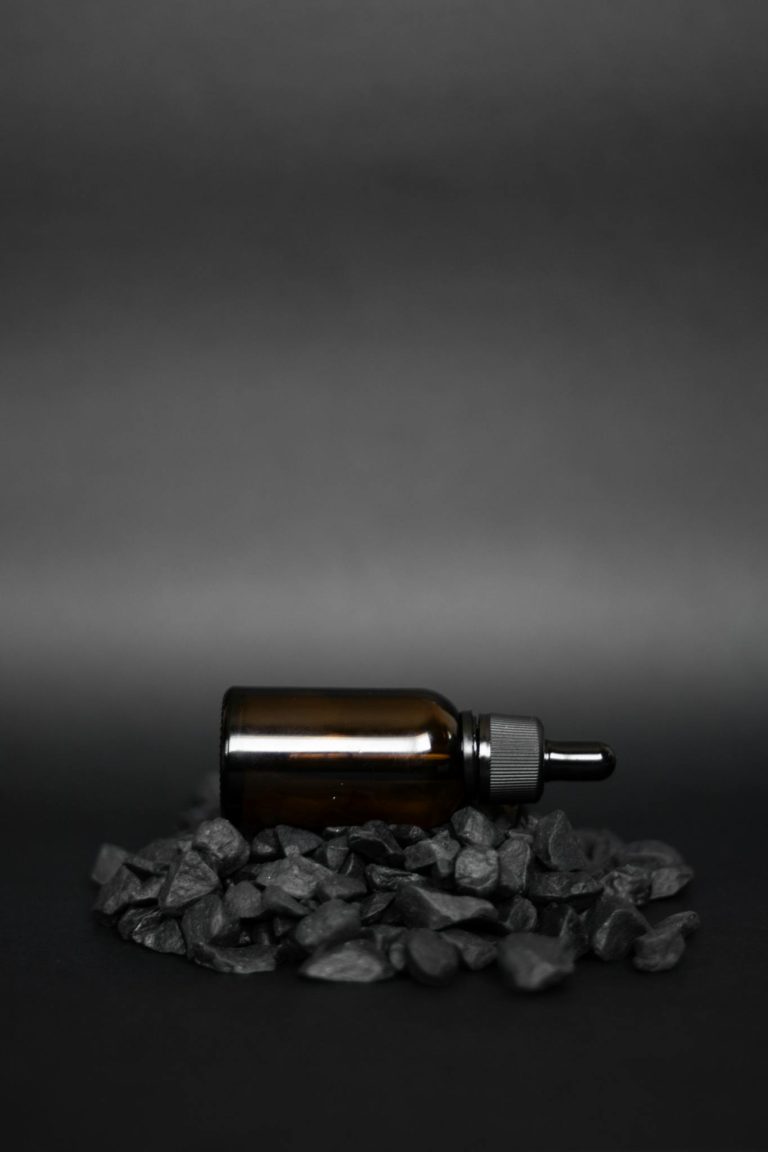 Elegant dark glass dropper bottle on black stones, showcasing luxury product photography.