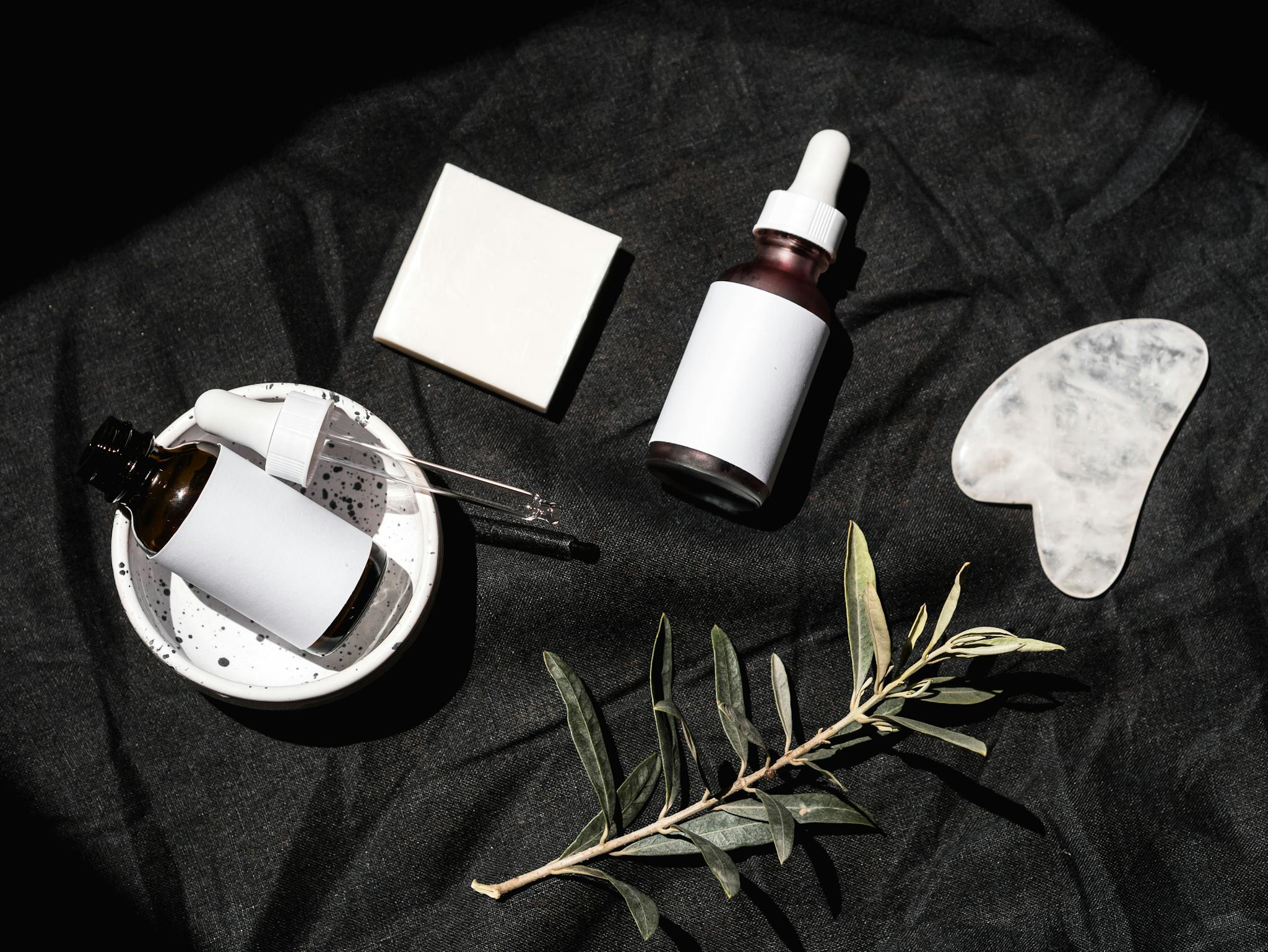 Flat lay of skincare bottles and leaves on black fabric. Perfect for beauty and wellness themes.